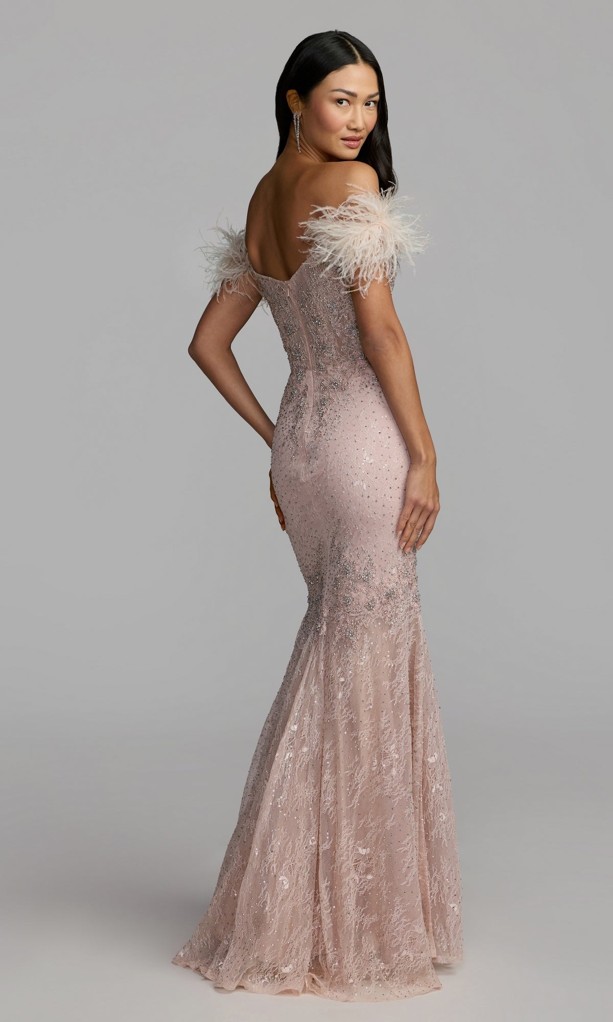 A woman wearing the Mac Duggal 20246 Off-Shoulder Long Formal Dress in blush, featuring lace accents and feathered off-the-shoulder sleeves, looks over her shoulder.